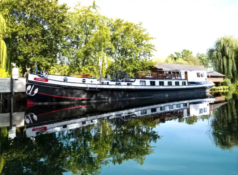 Hotel barge moored in Brittany, bordered by trees and showing reflection in the water.