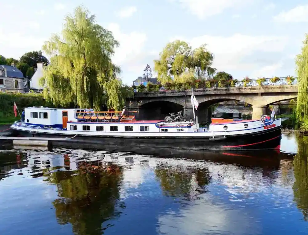 Hotel barge moored next to a stone bridge in town in Brittany